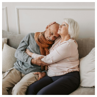 An elderly couple sharing a warm embrace on a cozy couch, displaying love and affection.